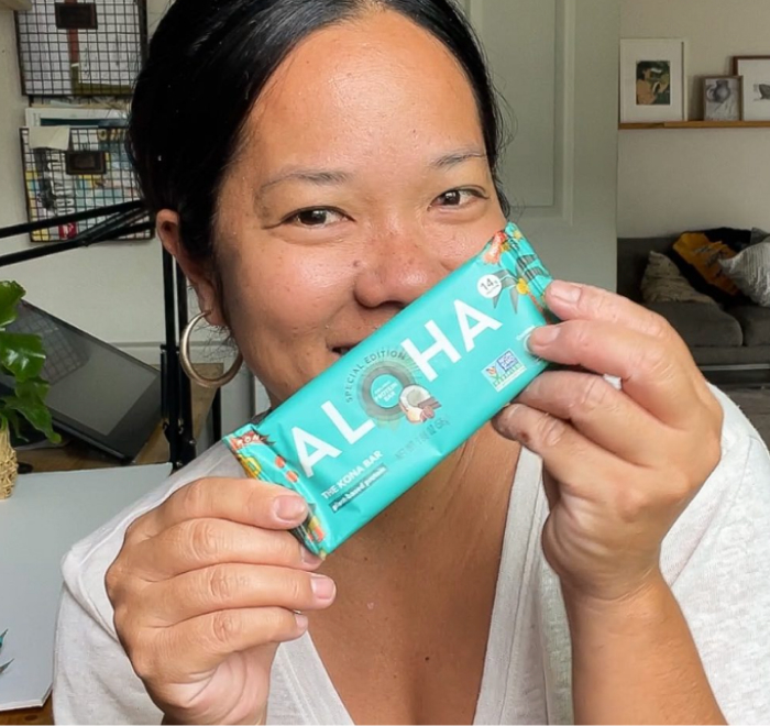 Person smiling and holding a turquoise bar labeled 'Aloha.'