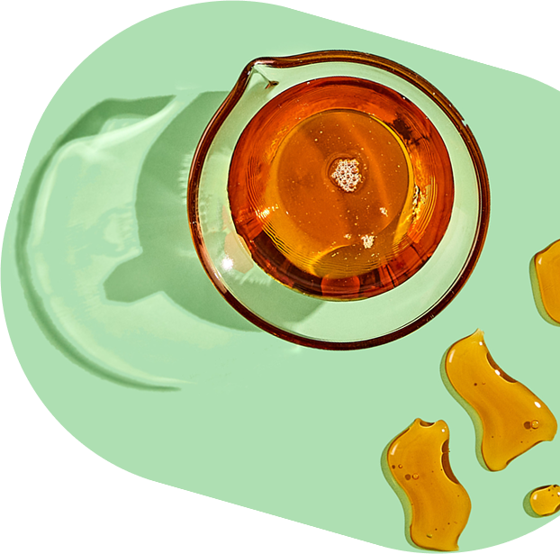 Glass container with amber liquid on a green background.