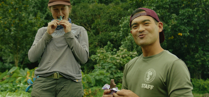 Two people enjoying snacks in a lush green outdoor setting.