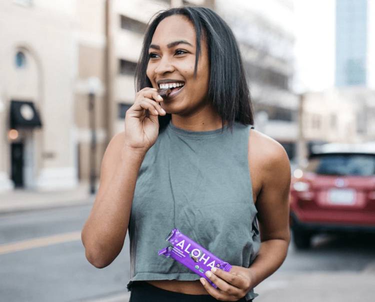 a woman is eating a aloha bar on the street