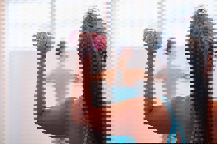 a woman in a blue tank top is lifting a pink dumbbell